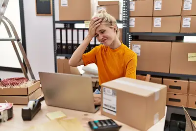 Young blonde woman working at small business ecommerce using laptop stressed with one hand on head, surprised and angry face